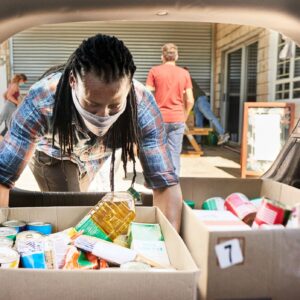 Young man in a face mask taking food donations from a car trunk