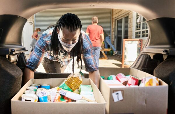 Young man in a face mask taking food donations from a car trunk